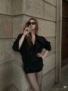 Woman in a black outfit and sunglasses drinking from a glass outdoors