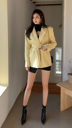 Woman in a yellow belted blazer, black top, and black skirt standing indoors