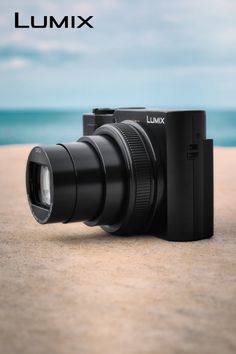 Black digital camera on a sandy surface with the ocean in the background
