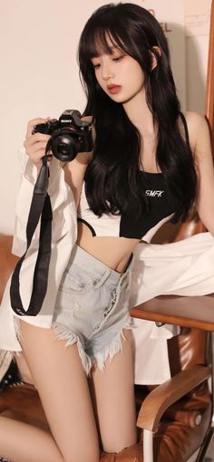 Woman with long black hair in a crop top and denim shorts holding a camera
