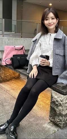 Woman with short hair in a grey jacket and black skirt sitting outdoors
