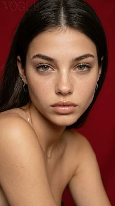 Woman with dark hair and green eyes against a red background