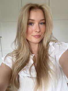 Woman with long blonde hair and blue eyes wearing a white shirt indoors