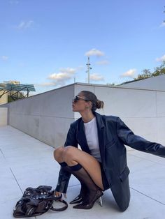 Woman in a leather jacket and high heels crouching outdoors