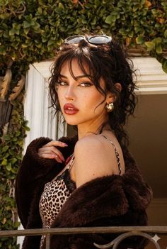 Woman with dark curly hair and red lipstick wearing a leopard print top and fur coat