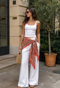 Woman in a white tank top and wide leg pants with a silk scarf tied around her waist