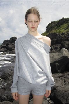 Young woman in a grey sweatshirt and shorts on a rocky beach