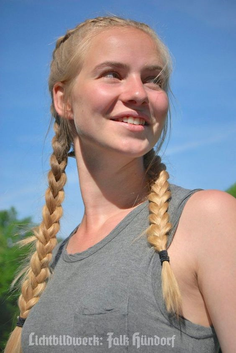 Young woman with blonde braids smiling outdoors under a blue sky