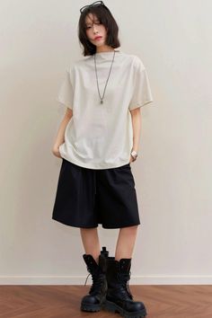 Woman with short hair wearing a white t-shirt, black shorts, and combat boots