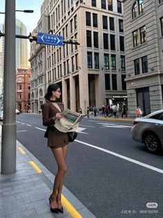 Woman in a brown suit and high heels standing on a city street holding a newspaper