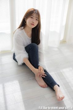 Woman with long hair wearing a white fluffy sweater and jeans, sitting on the floor