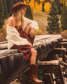 Woman in a cowboy hat and plaid dress sitting on a wooden bridge in autumn