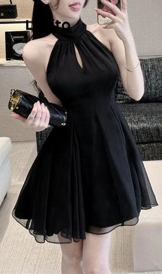 Woman in a black halter neck dress holding a clutch bag indoors