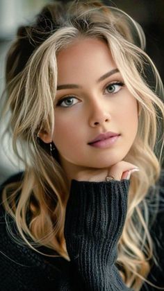 Woman with blonde hair wearing a black sweater, resting her chin on her hand