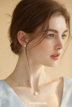 Woman with blue eyes and brown hair wearing pearl earrings and a gold necklace