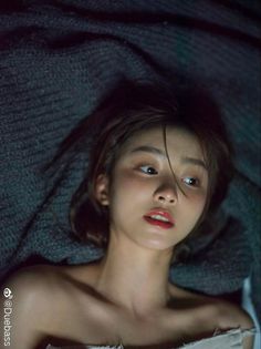 Woman with short hair and exposed shoulders lying on a dark blanket