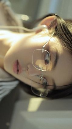 Close up of a woman with glasses and long hair, lying down with soft lighting
