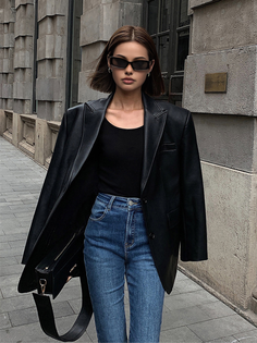 Woman with short hair and sunglasses wearing a leather jacket and jeans on a street