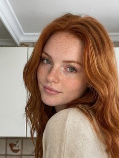 Woman with red hair and freckles looking at the camera indoors