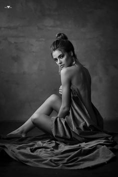 Woman with an updo and long earrings, draped in fabric, in a dramatic black and white photograph
