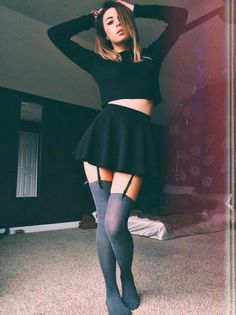 Woman in a black crop top and mini skirt with thigh high socks and garter straps