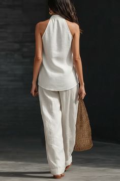 Woman in a white halter top and wide leg pants holding a straw bag