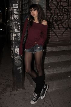 Woman in an off-shoulder top, denim shorts, and tights on a dark street