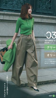 Woman in a green polo shirt and wide leg pants holding a green jacket and wicker bag