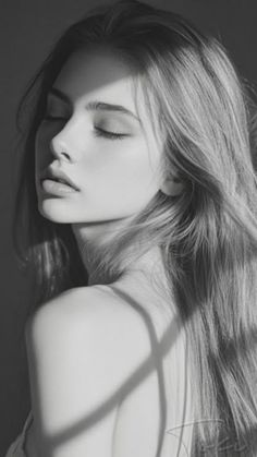 Monochrome portrait of a woman with long hair and closed eyes, with shadows on her face and shoulder