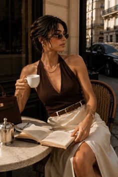 Woman in a halter top and skirt reading a book at an outdoor cafe