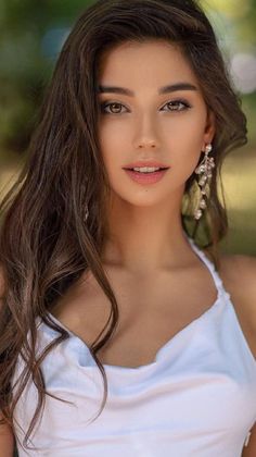 Woman with long brown hair wearing a white top and dangle earrings