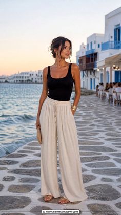 Woman in a black tank top and wide leg pants in a coastal town at sunset