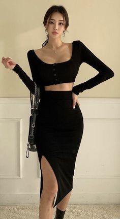 Woman in a black long-sleeve crop top and high-slit midi skirt posing indoors