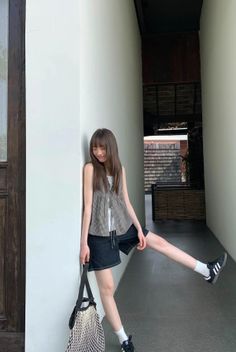Woman with long hair in denim shorts and a sleeveless top leaning against a wall