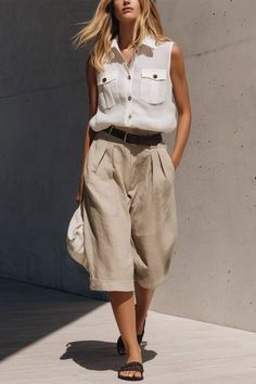 Woman with blonde hair wearing a white sleeveless shirt and khaki pants outdoors