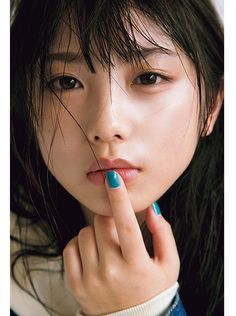 Woman with black hair and blue nail polish with a finger on her lips