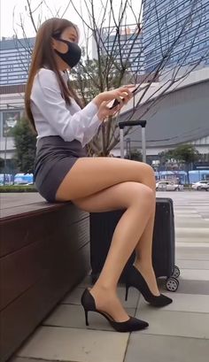 Woman in a white shirt and mini skirt sitting outdoors with a suitcase