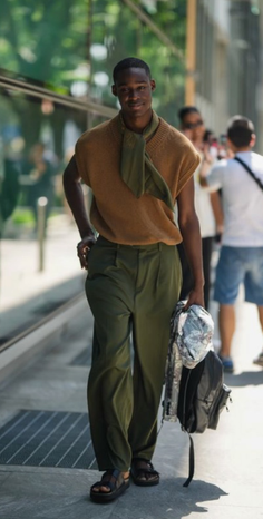 Man in a brown sleeveless sweater and green pants walking outdoors
