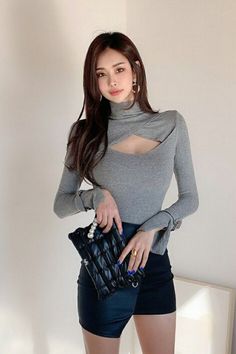 Woman in a gray cutout top and black skirt holding a clutch bag