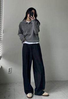Person in a gray sweater and wide leg pants taking a mirror selfie indoors