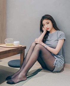 Woman in a gray dress and black tights sitting on the floor indoors
