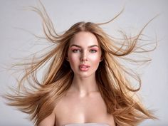 Woman with long blonde hair flying around her face, wearing pink makeup