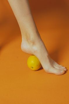 Bare foot resting on a lemon against an orange background