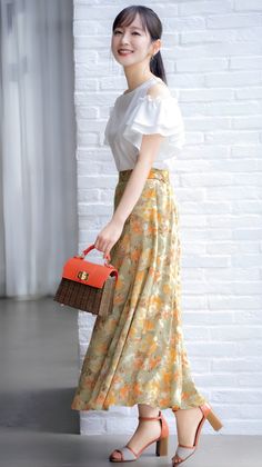 Woman in a floral skirt and white blouse holding an orange handbag