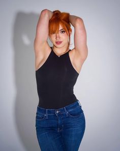 Woman with red hair in a black top and blue jeans posing indoors