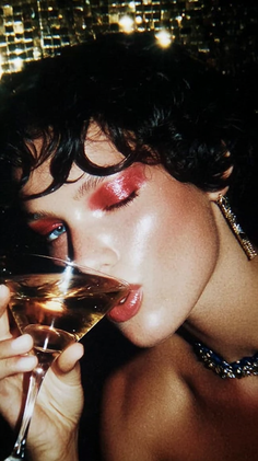 Woman with red eyeshadow drinking from a cocktail glass at night