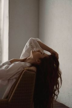 Woman with long hair in a white shirt reclining indoors