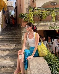 Woman in a white tank top and blue skirt sitting on a stone wall outdoors
