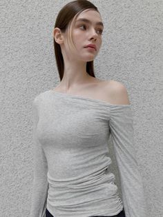Woman with long hair wearing an off-shoulder top against a light gray wall