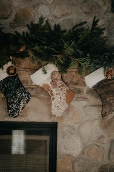Christmas stockings with cowhide patterns hanging on a stone fireplace with evergreen garland